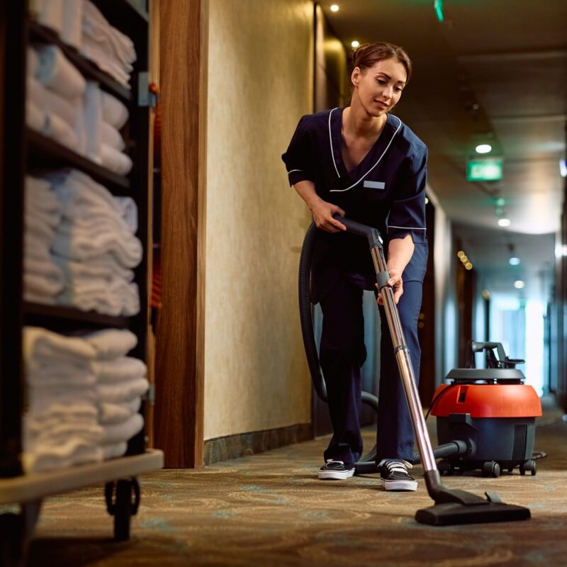Young cleaning lady vacuuming hotel hallway.